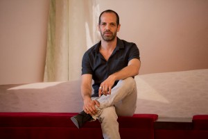 Der Schauspieler Yousef Sweid. Im Hintergrund die Fotografie von Sven Johne: "Traumhotels (Lampedusa)", Fotoserie 2012. Foto (c) Judith Buss.